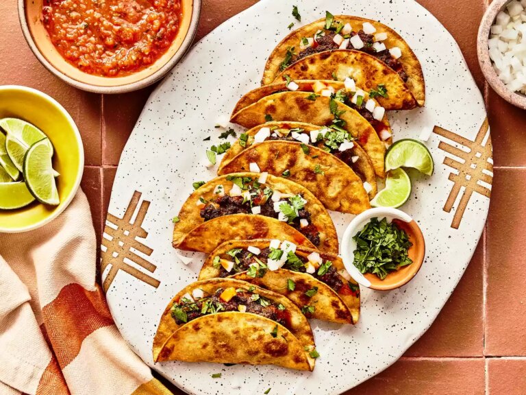 An overhead view looking down on a platter of fried beef tacos served garnished with onion and cilantro.