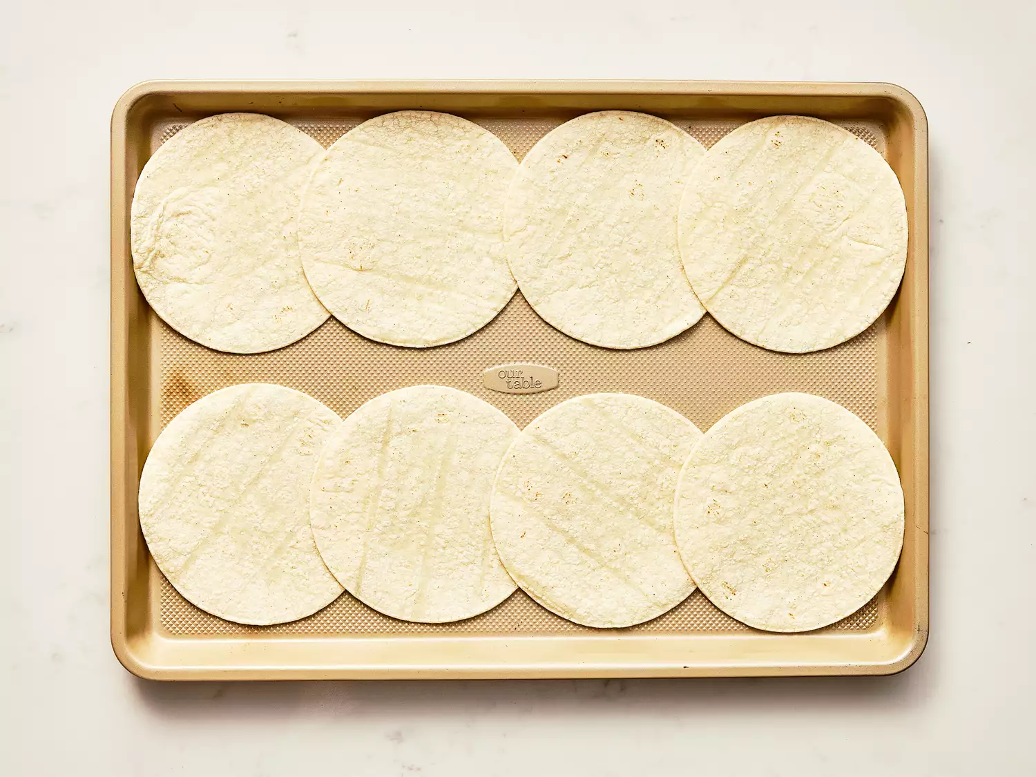 eight flour tortillas lined up on a baking sheet. 