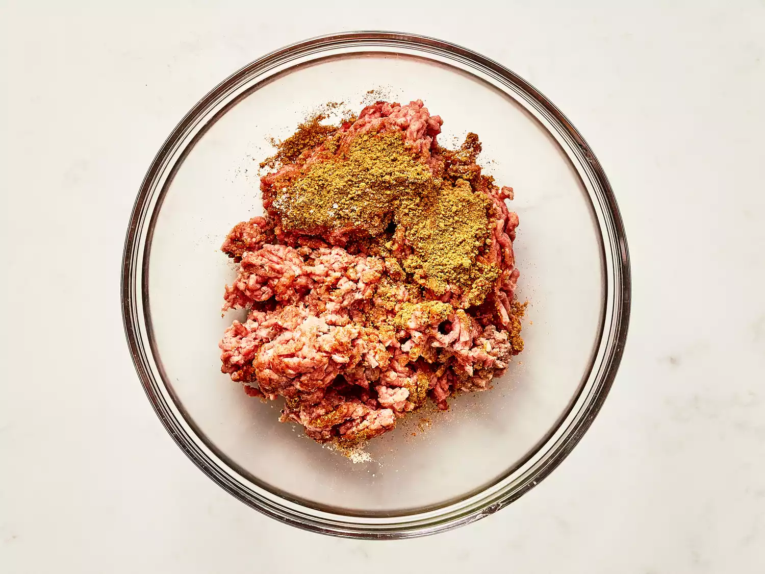 ground beef in a glass mixing bowl with taco seasoning added. 