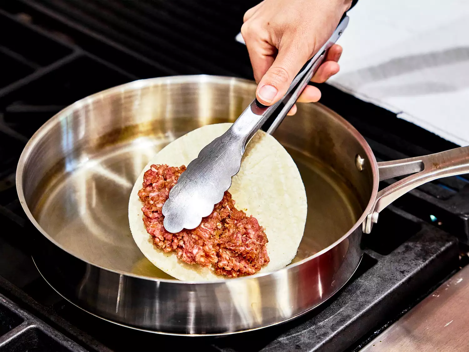 tortilla with ground beef being added to a shallow pan of oil for frying. 