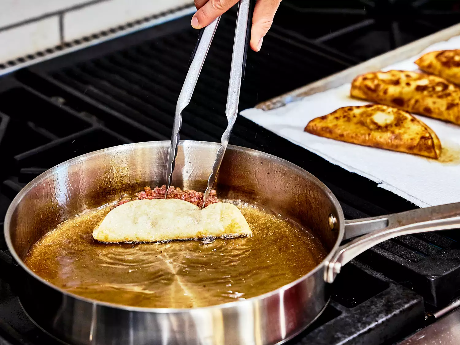 ground beef taco, folded in half, frying in a shallow pan.