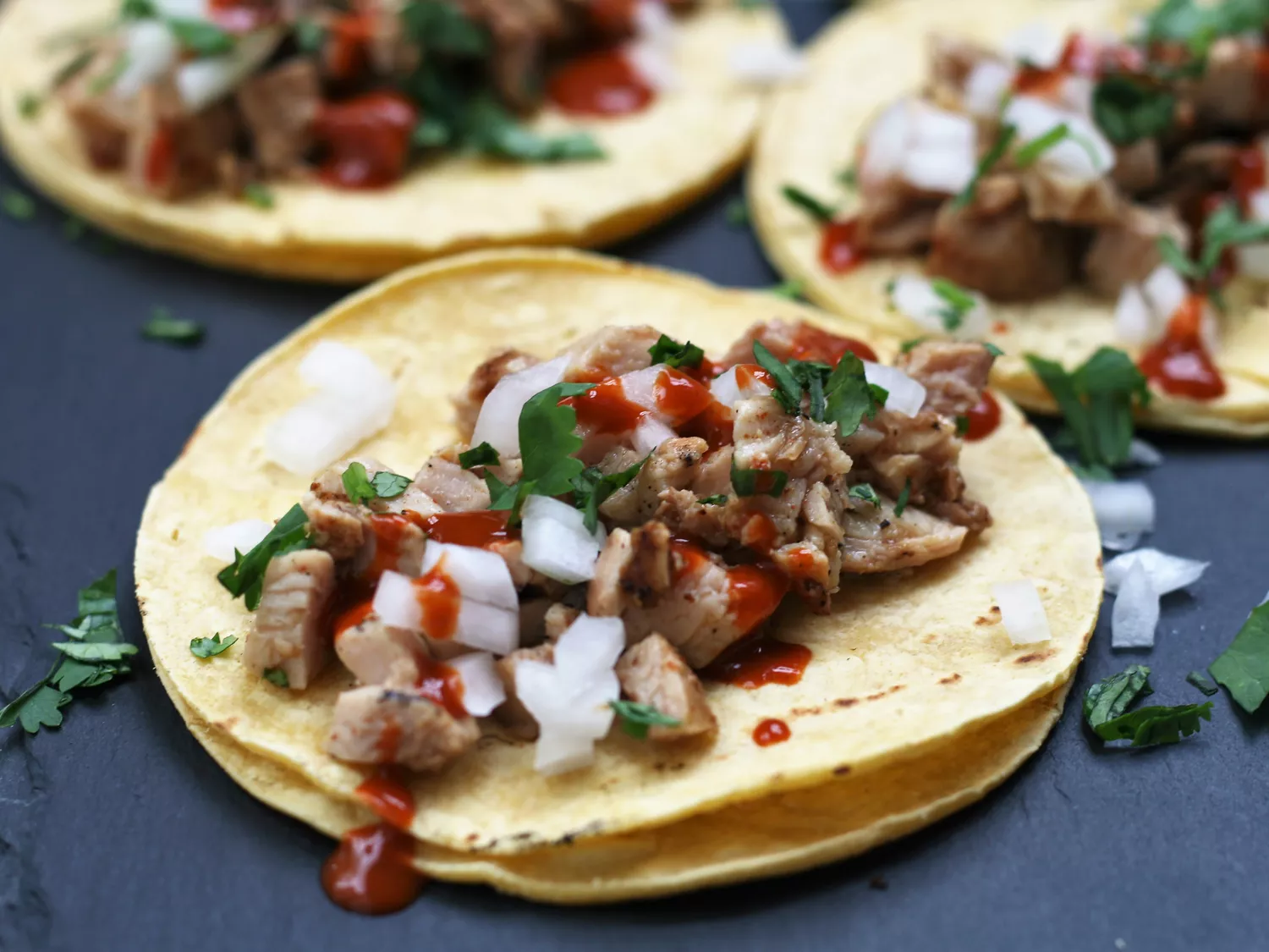 Closeup of grilled chicken tacos with chopped onion and cilantro on blue grey plate