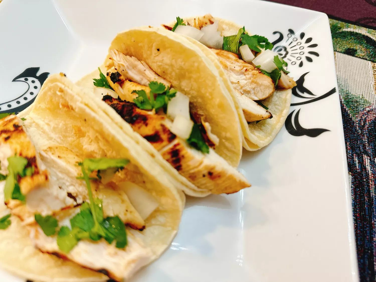 Grilled chicken, chopped onion, and cilantro in street taco size corn tortillas on white plate