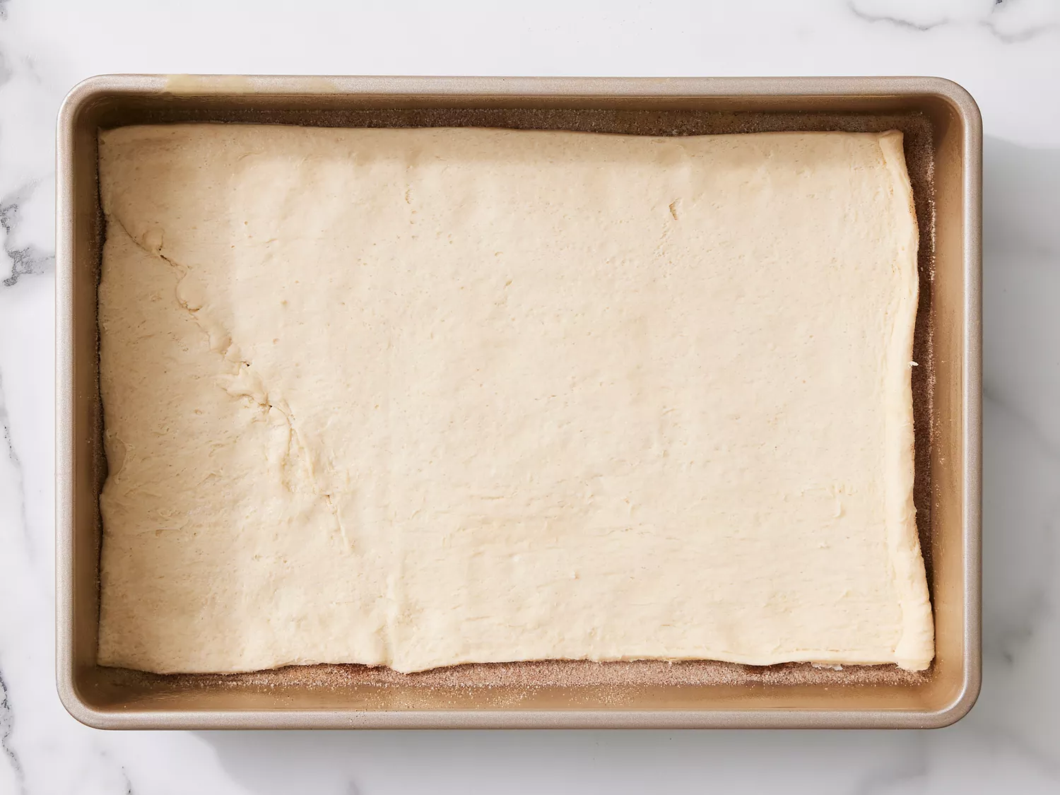 crescent dough rolled out and placed over cinnamon sugar in a baking pan. 