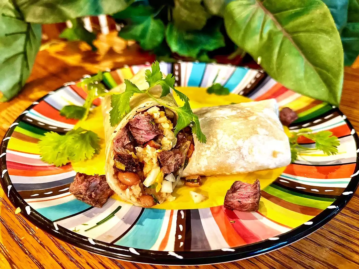 Colorful plate with halved burrito filled with steak, beans, and rice, garnished with cilantro