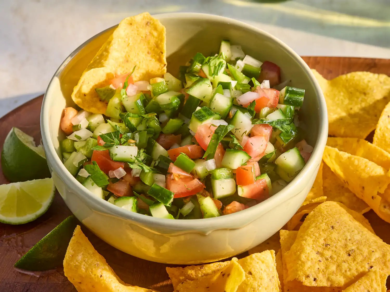 Bowl of cucumber salsa with tortilla chips, garnished with lime wedges