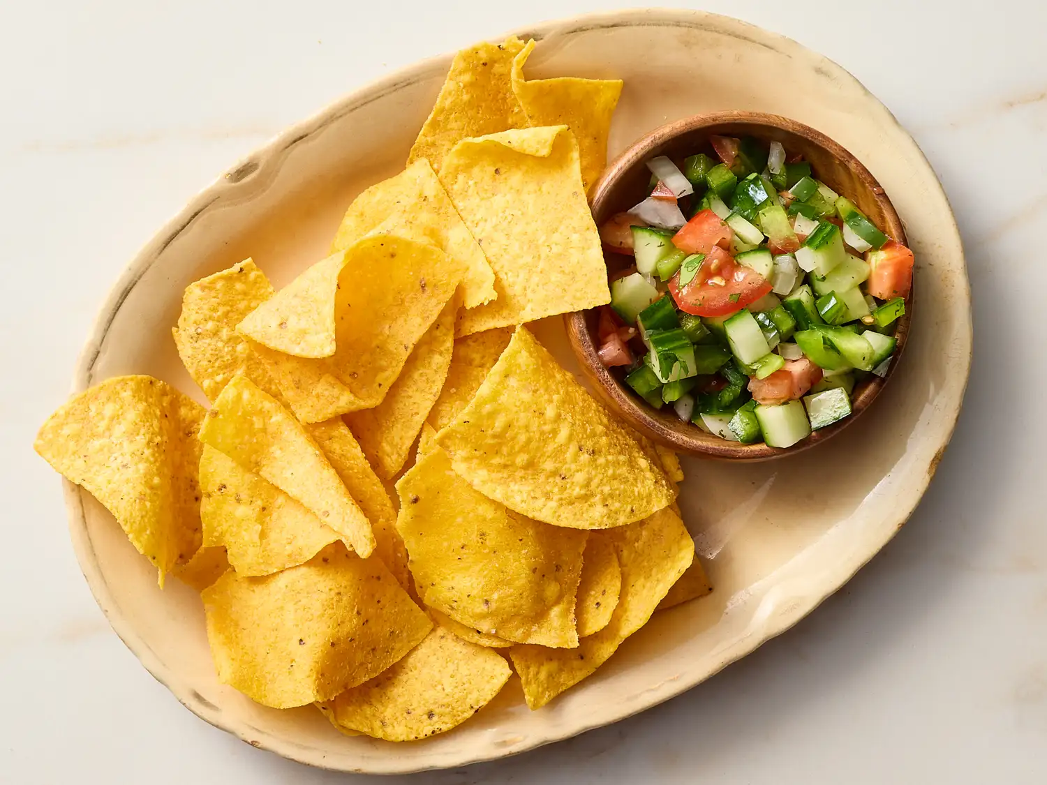 A dish with tortilla chips and a bowl of cucumber salsa