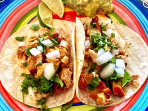 Overhead view of two chicken tacos on a colorful plate with limes and guacamole