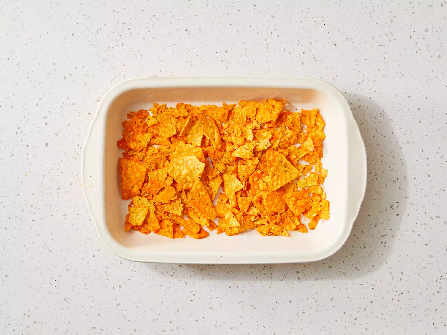 a 9x13 casserole dish layered with broken nacho Dorito chips.