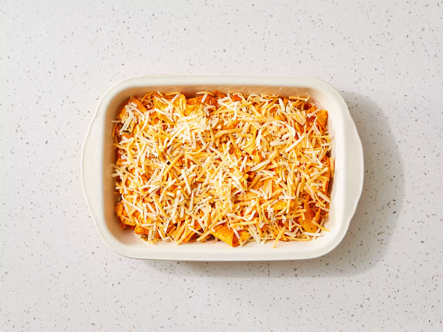 Dorito casserole topped with shredded cheese before baking. 