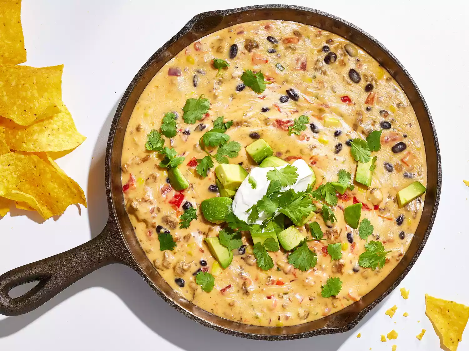 Campfire queso in a cast iron skillet topped with diced avocado, cilantro, and sour cream.