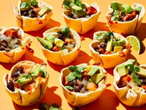 Several sweet potato and black bean taco cups on a yellow surface.