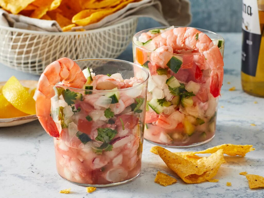 Close up on two small cups of mexican ceviche, served with chips and a beer.