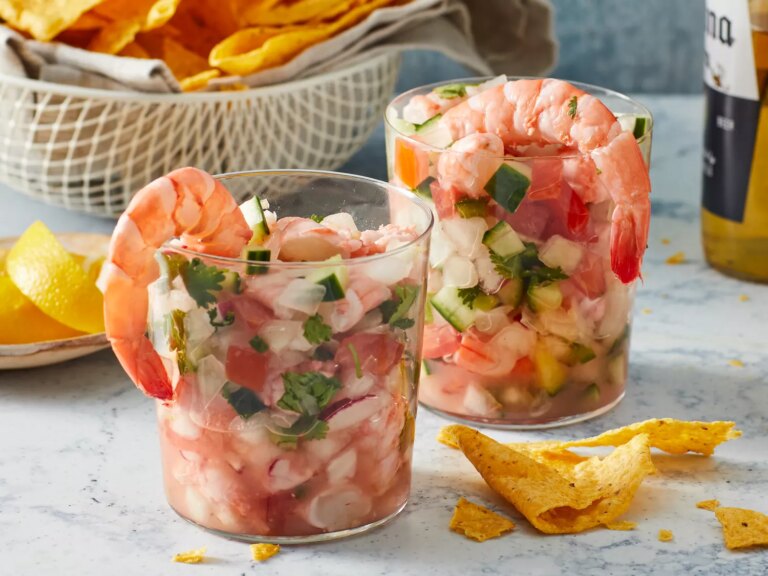 Close up on two small cups of mexican ceviche, served with chips and a beer.