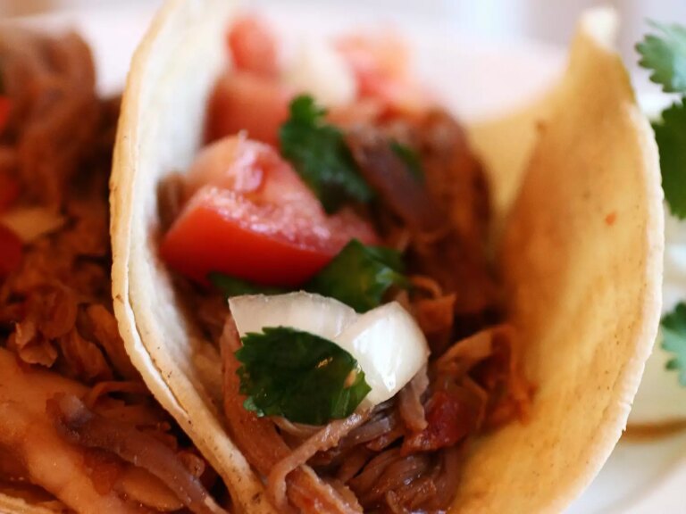 Close up view of sweet pork tacos with tomatoes, onions and herbs