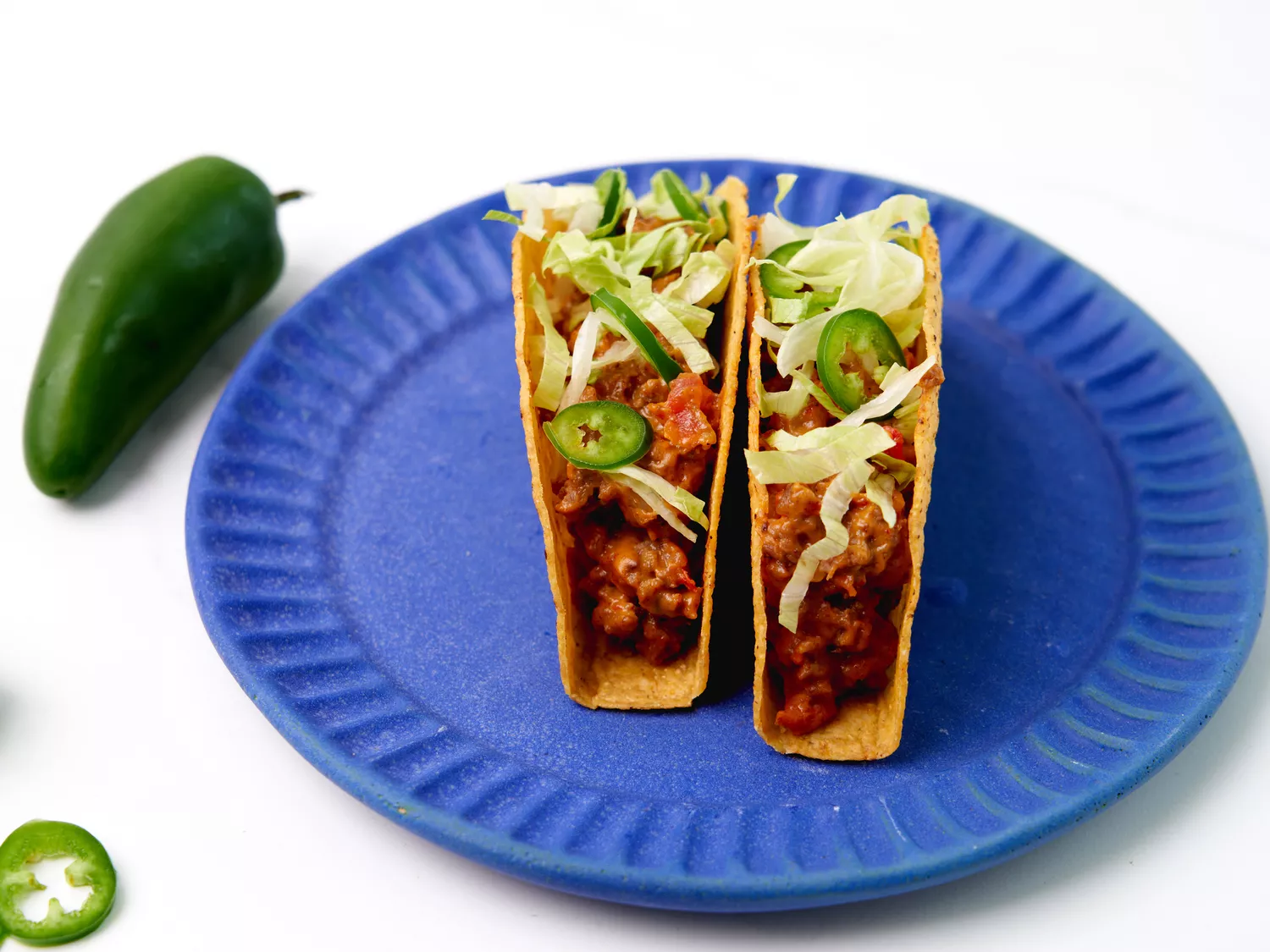 2 tacos filled with ground beef topped with lettuce and jalapenos