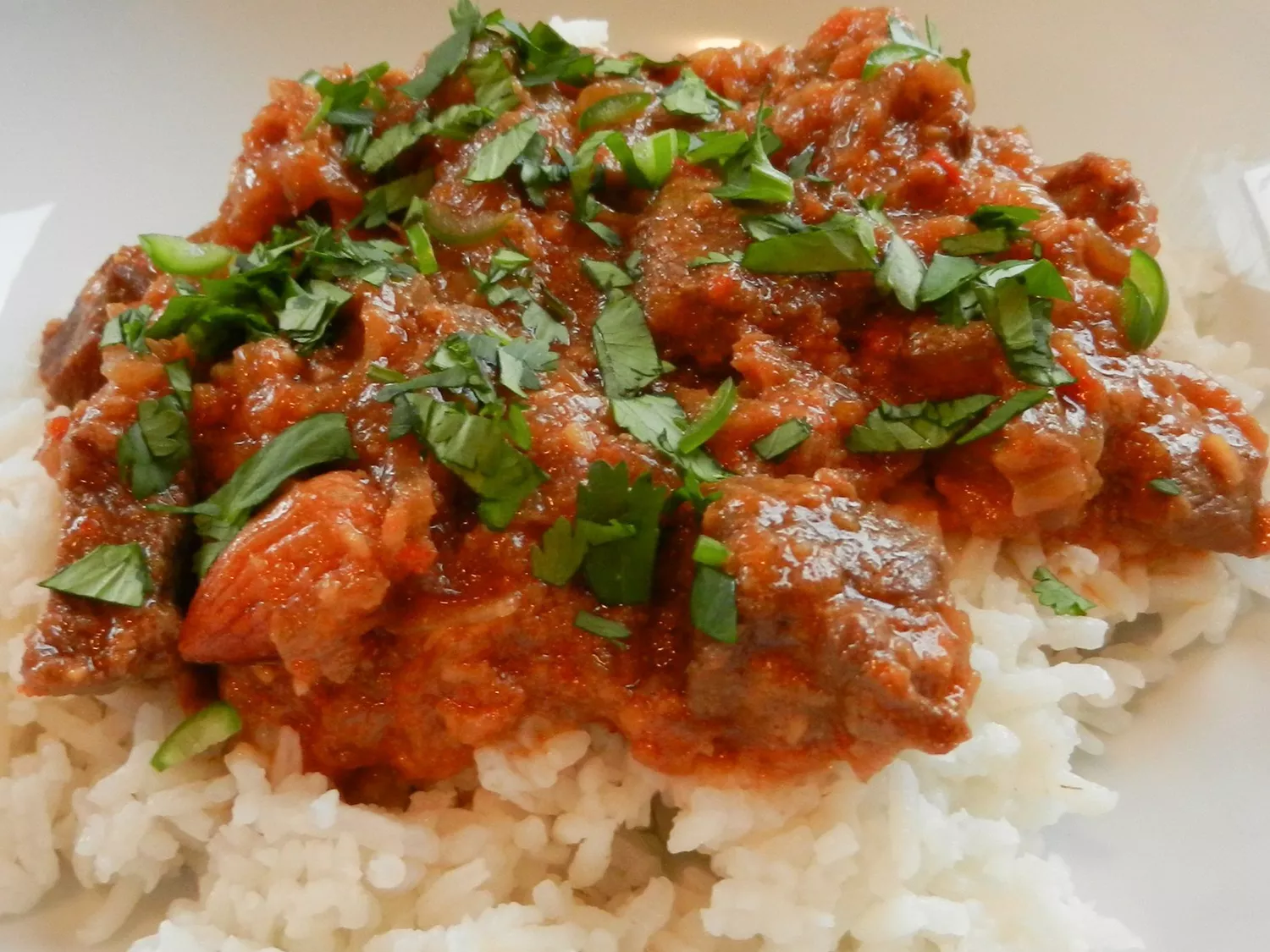Close up view of kashmiri lamb over white rice garnished with fresh herbs in a bowl