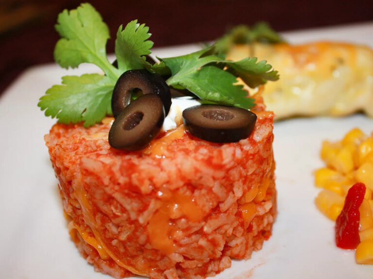 Close up view of taco rice garnished with black olive slices and fresh herbs on a white plate
