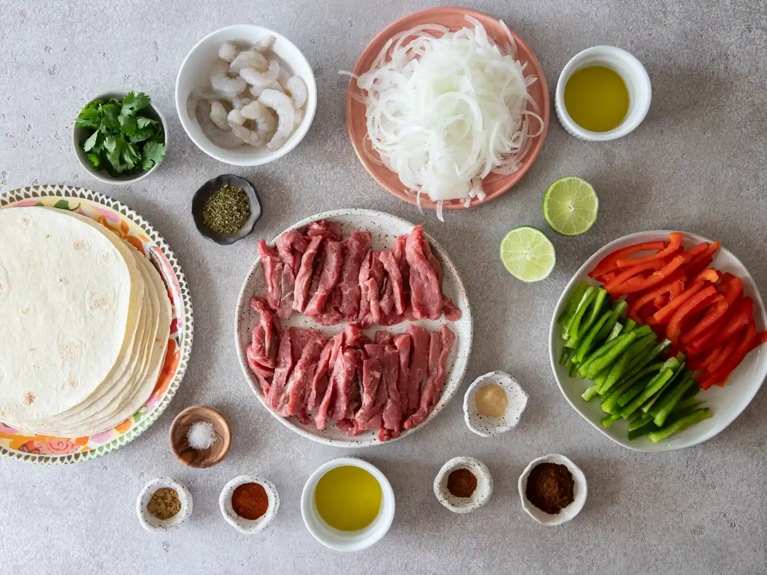 Ingredients arranged for steak and shrimp fajitas including tortillas beef slices shrimp bell peppers onions seasonings and olive oil