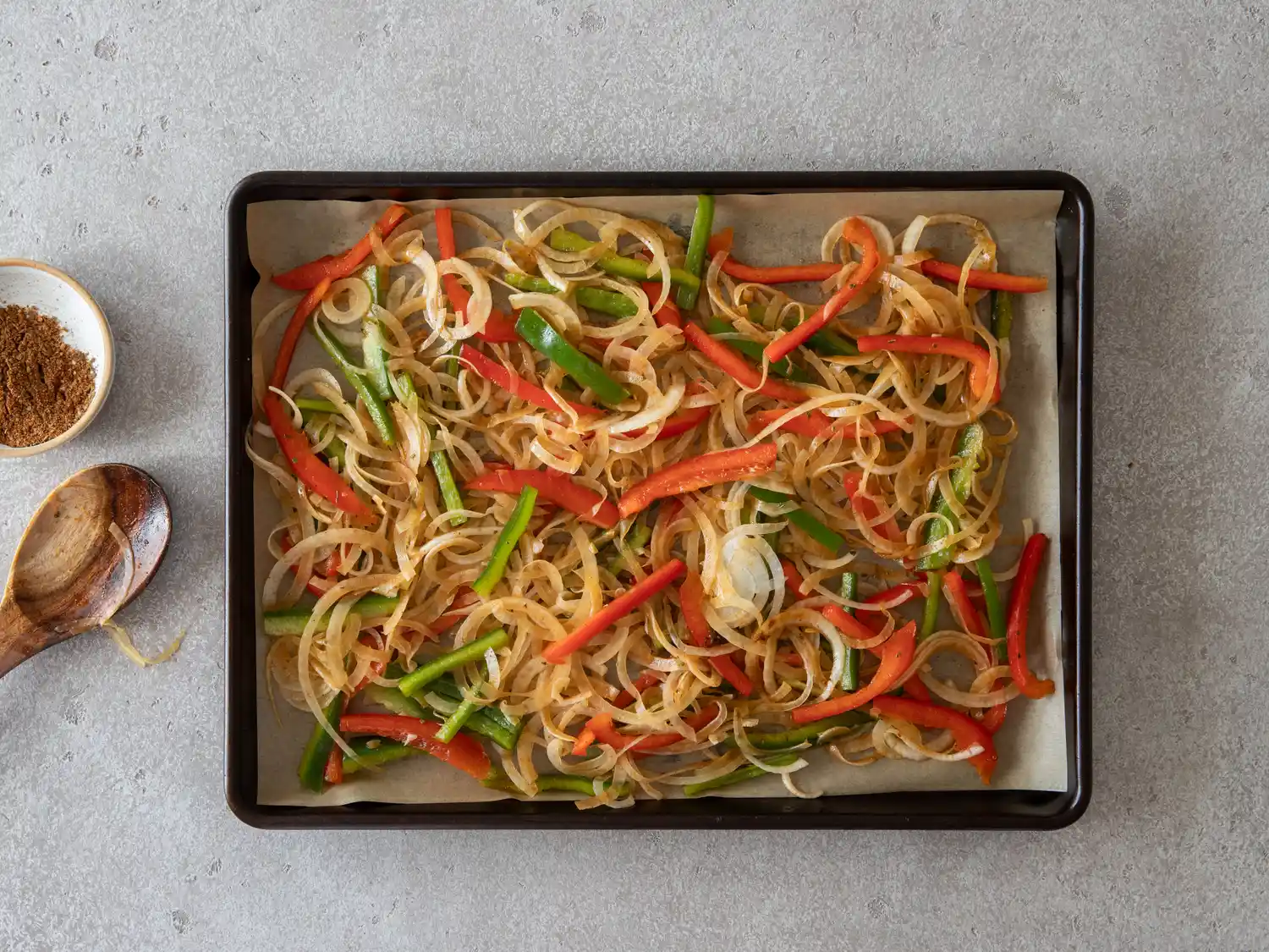A baking tray filled with sliced vegetables including onions red bell peppers and green beans prepared for cooking