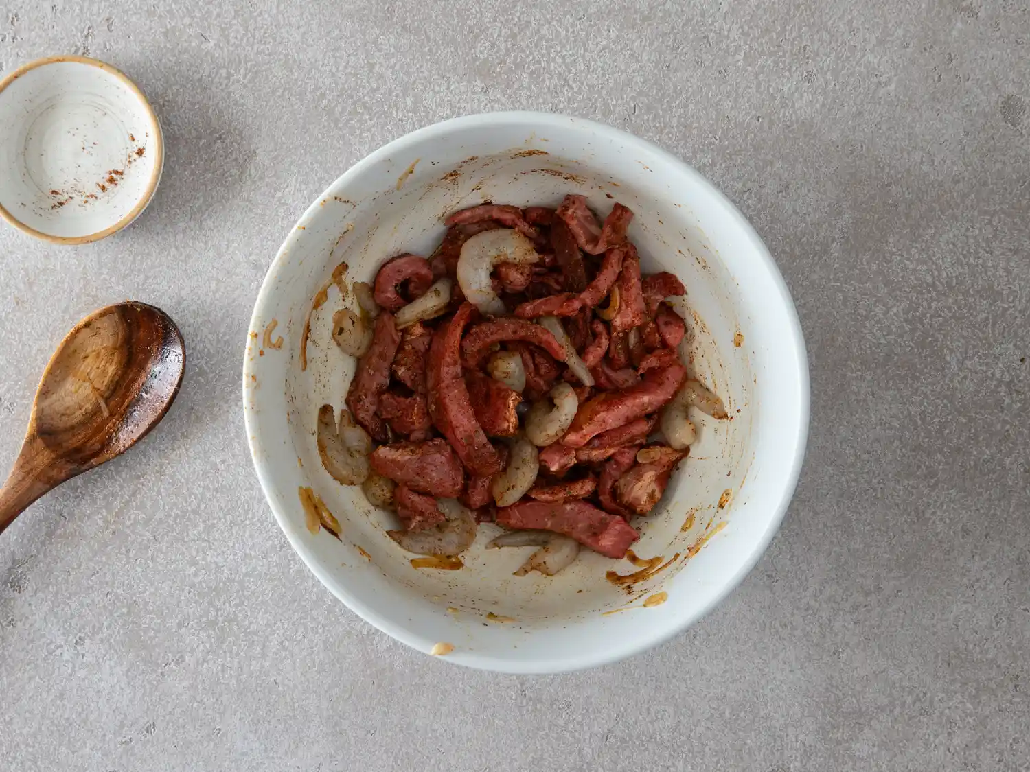 Bowl of seasoned steak and shrimp with a wooden spoon beside it