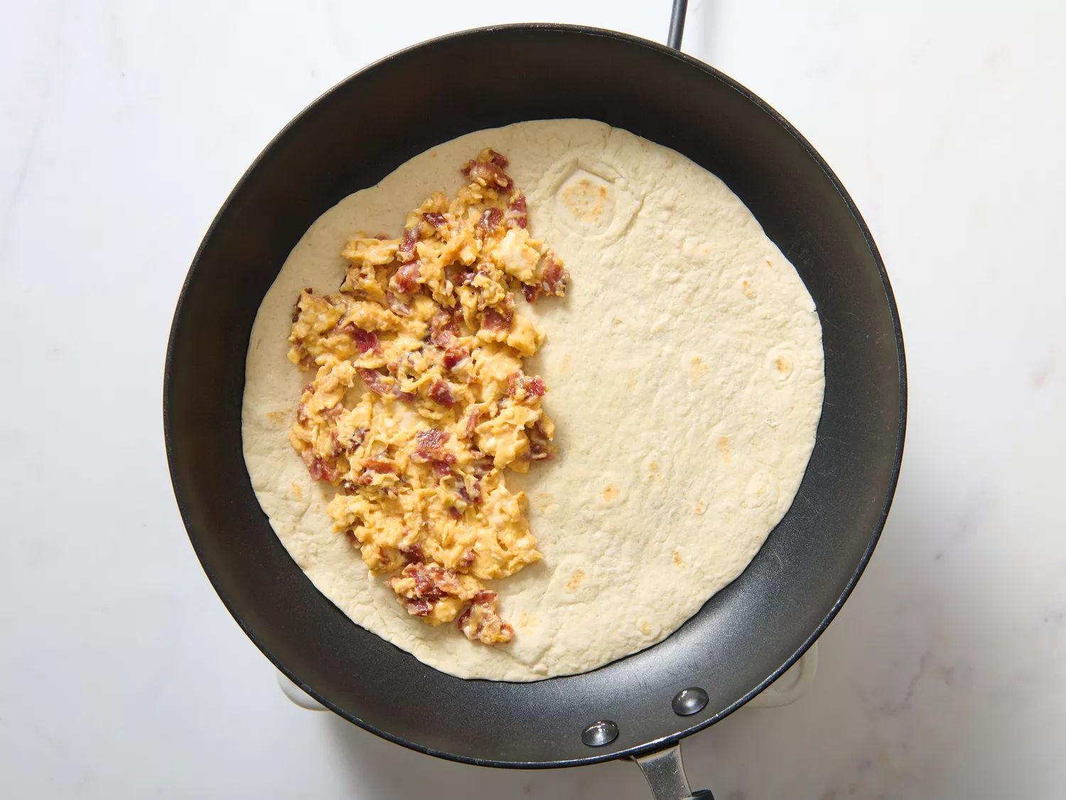 Quesadilla preparation in a frying pan with scrambled eggs and filling on one side of a tortilla
