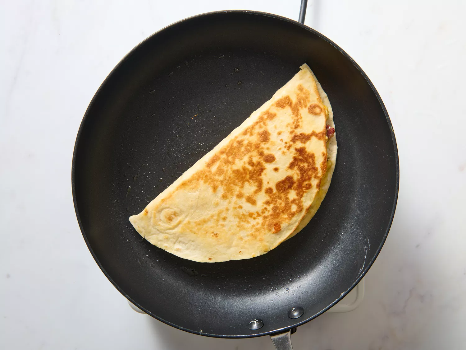Half-folded quesadilla in a skillet being cooked