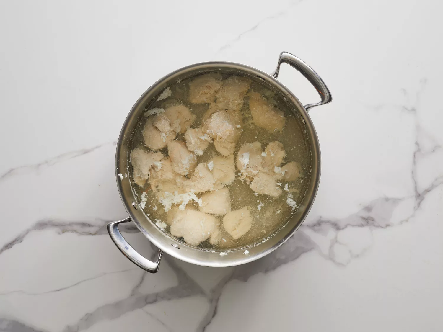 an overhead shot of chunks of chicken boiling in a pot of water