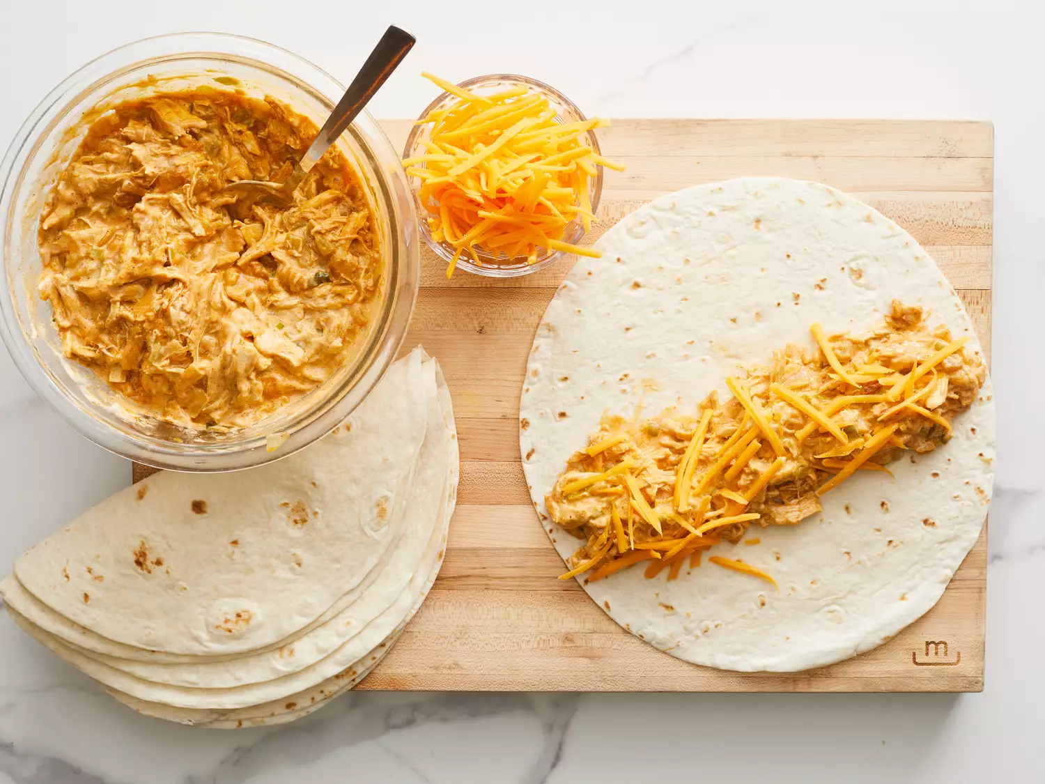 an overhead shot of chicken mixture and cheese in bowls and filling a tortilla on a cutting board
