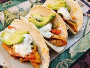 3 chicken fajita tacos topped with sour cream and avocado