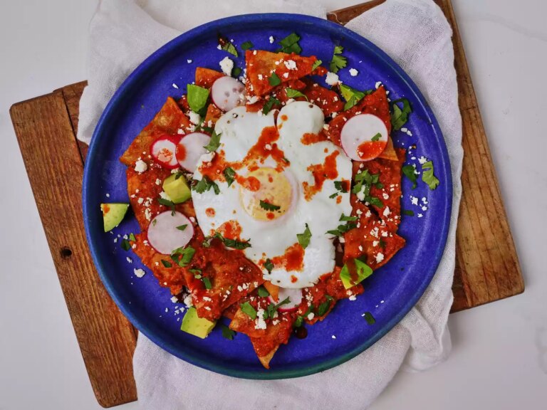 Bright blue plate with chilaquiles in red sauce, fried egg on top