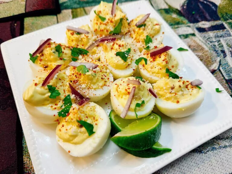 Square white plate of deviled eggs with red onion, cilantro, and lime wedges