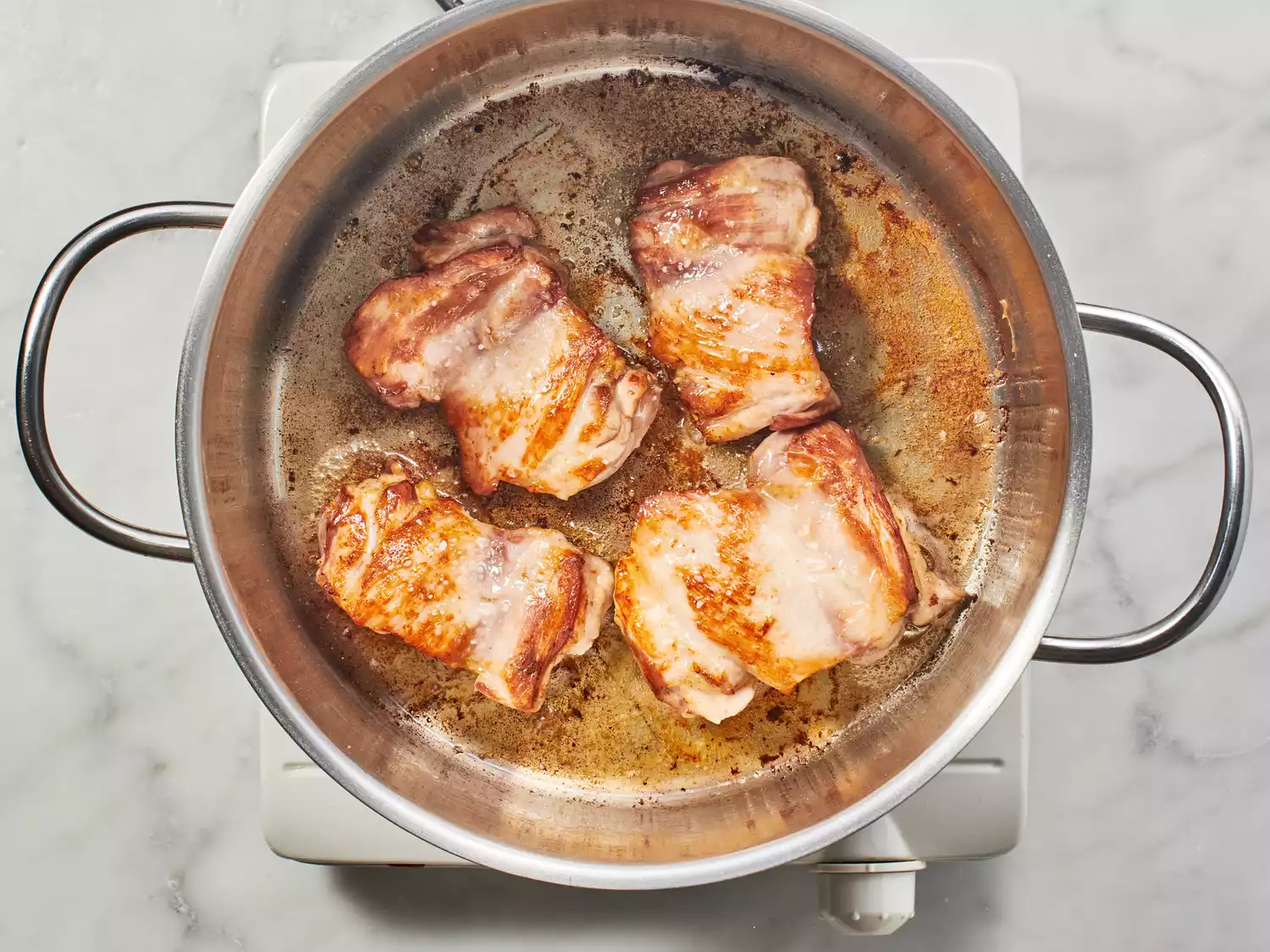 Chicken thighs browning in a stock pot.