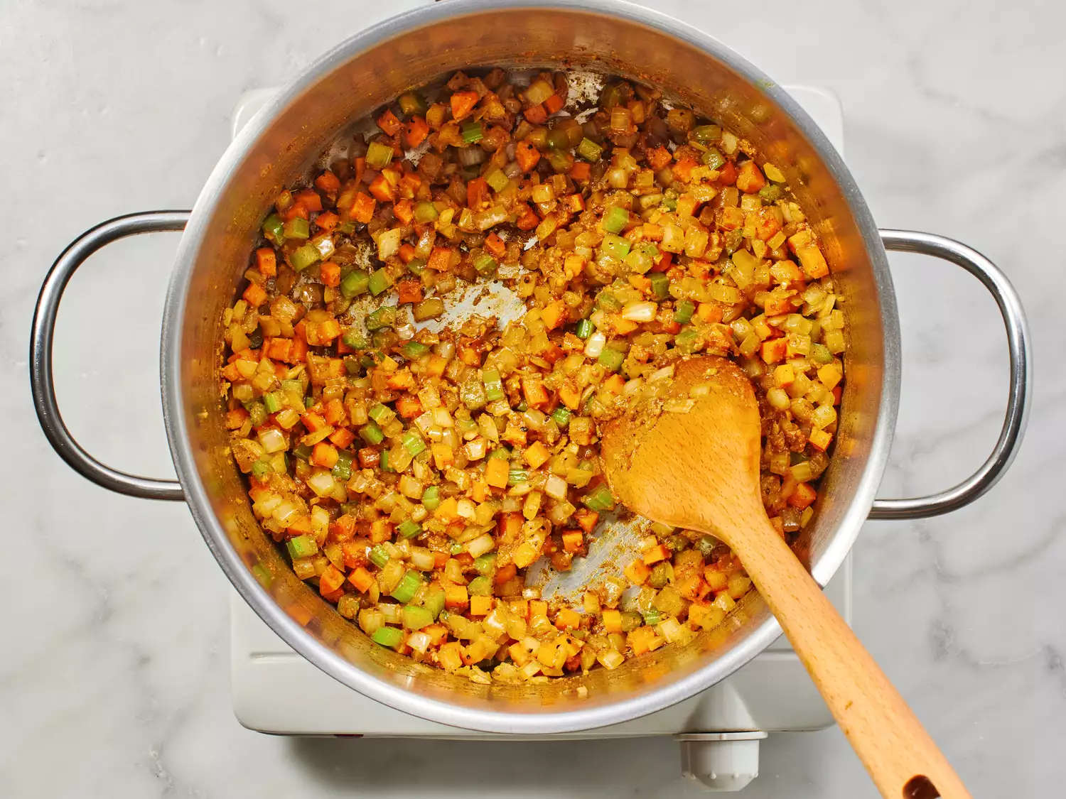 A wood spoon in a stock pot with diced vegetables and spices. 