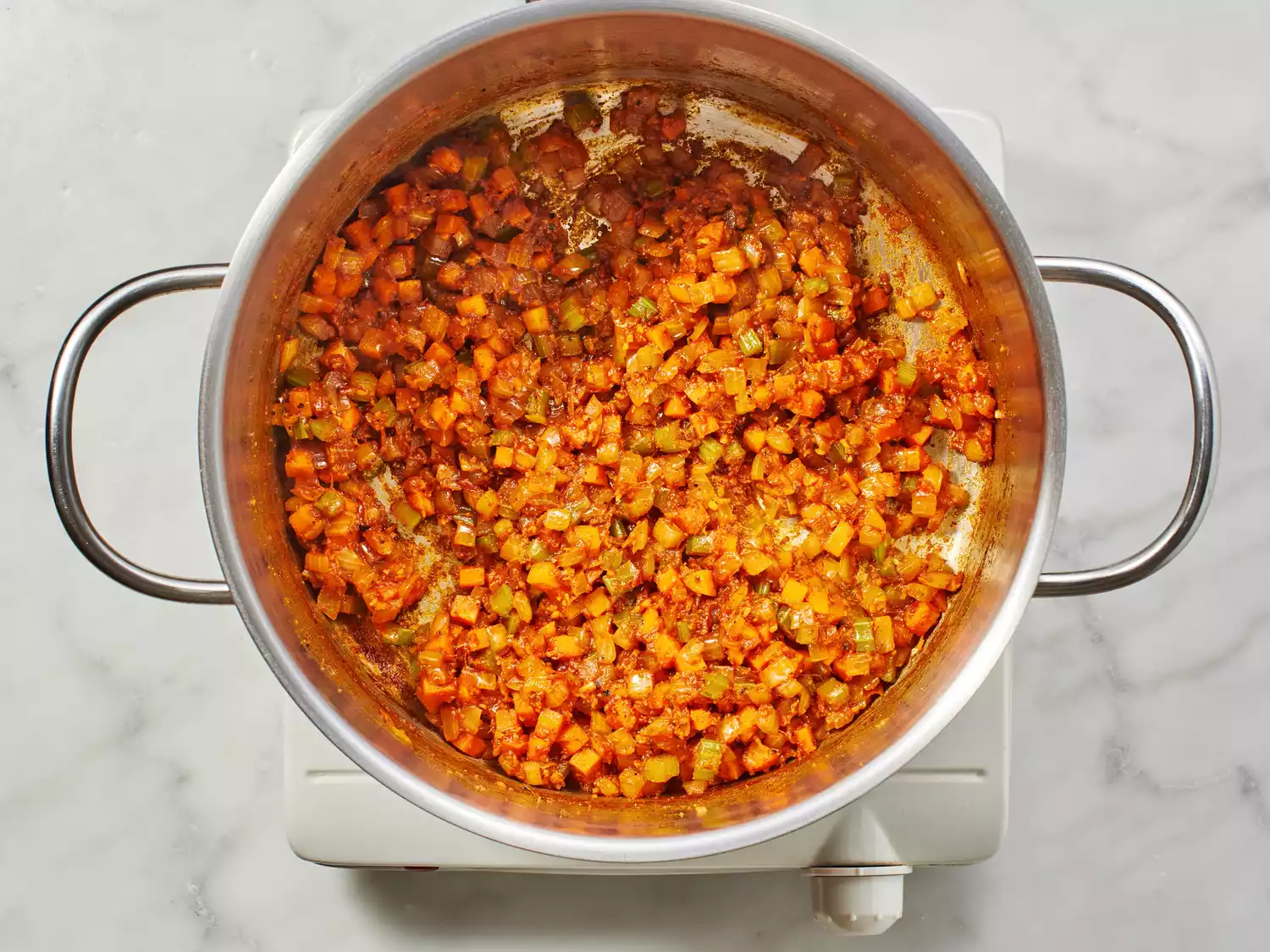 Diced vegetables with tomato paste and spices in a stock pot. 