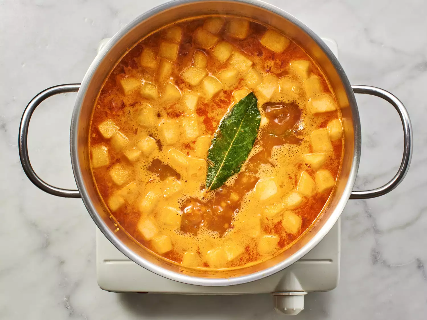 A pot with potatoes, bay leaf and stock. 