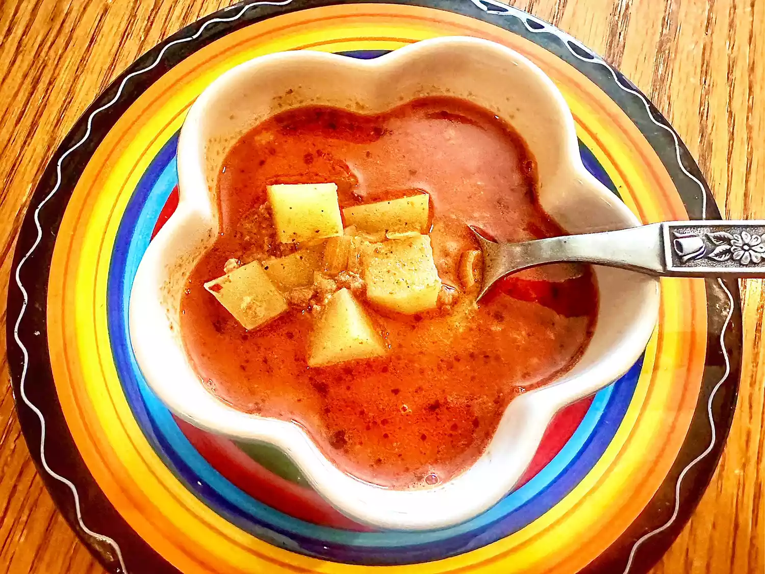 Bird's eye view of bowl of chorizo soup with potatoes on colorful charger