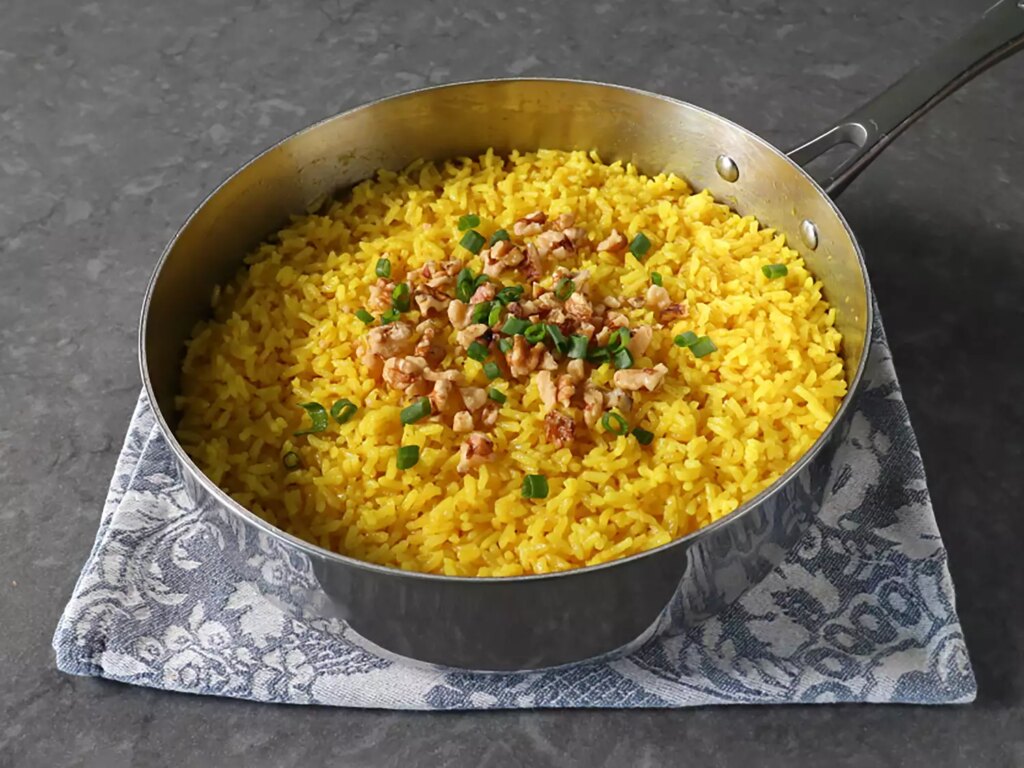 Saucepan with golden rice topped with walnuts and green onions