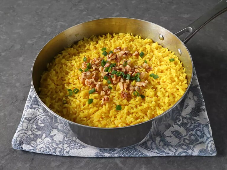 Saucepan with golden rice topped with walnuts and green onions