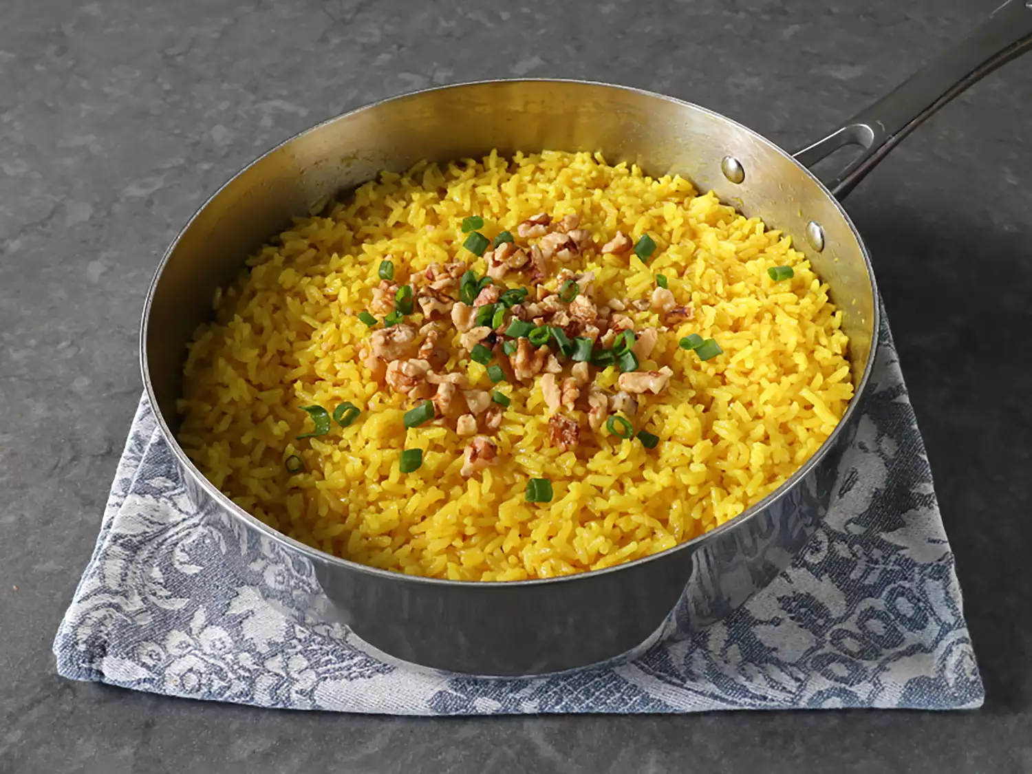 saucepan with golden rice topped with walnuts and green onions