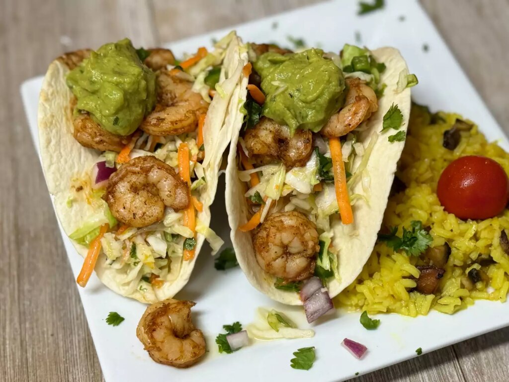 Overhead view of 2 shrimp tacos with guacamole and coleslaw on white plate