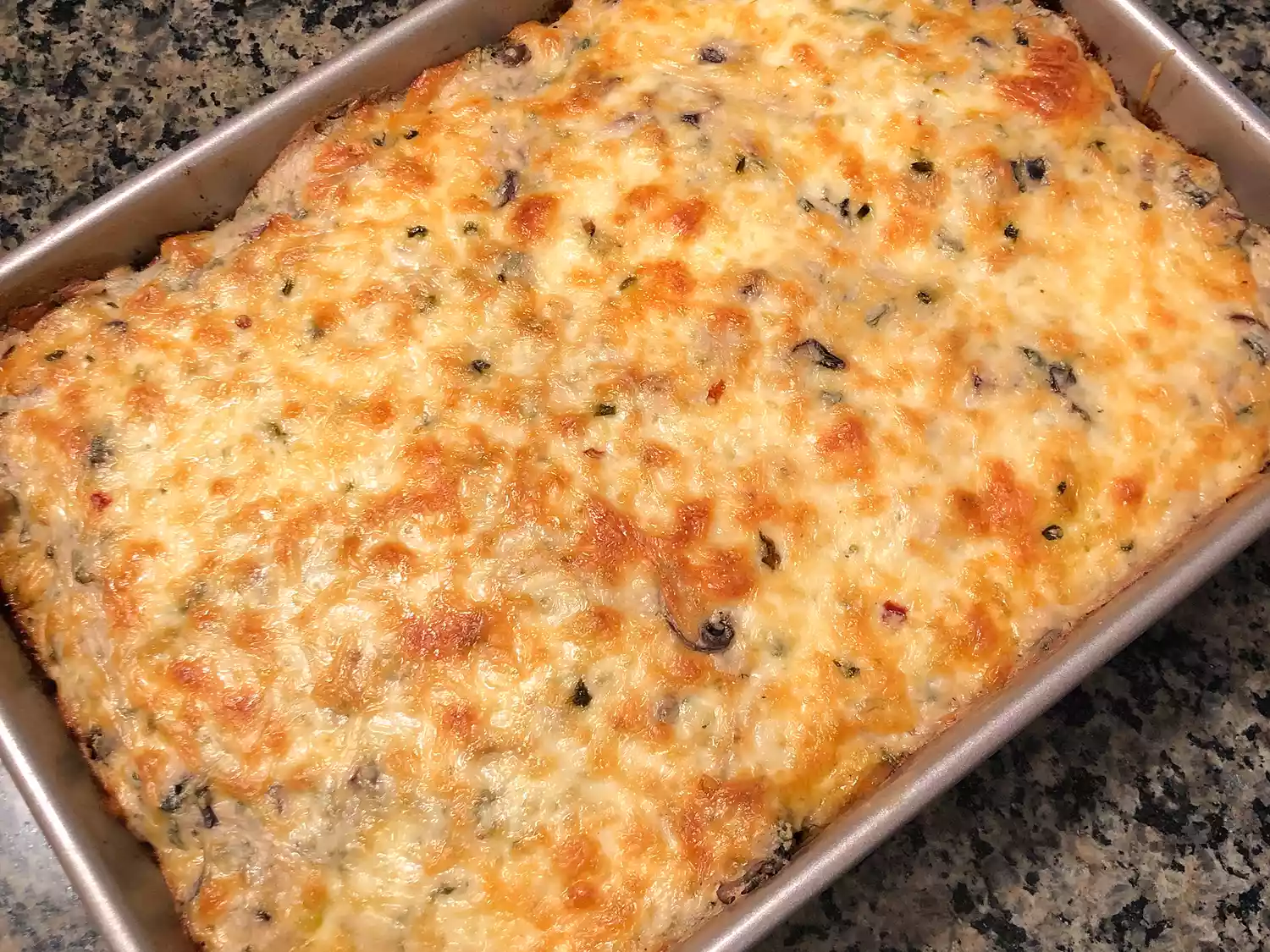 Close up view of a poblano chicken enchilada casserole with melted cheese on top, in a baking dish