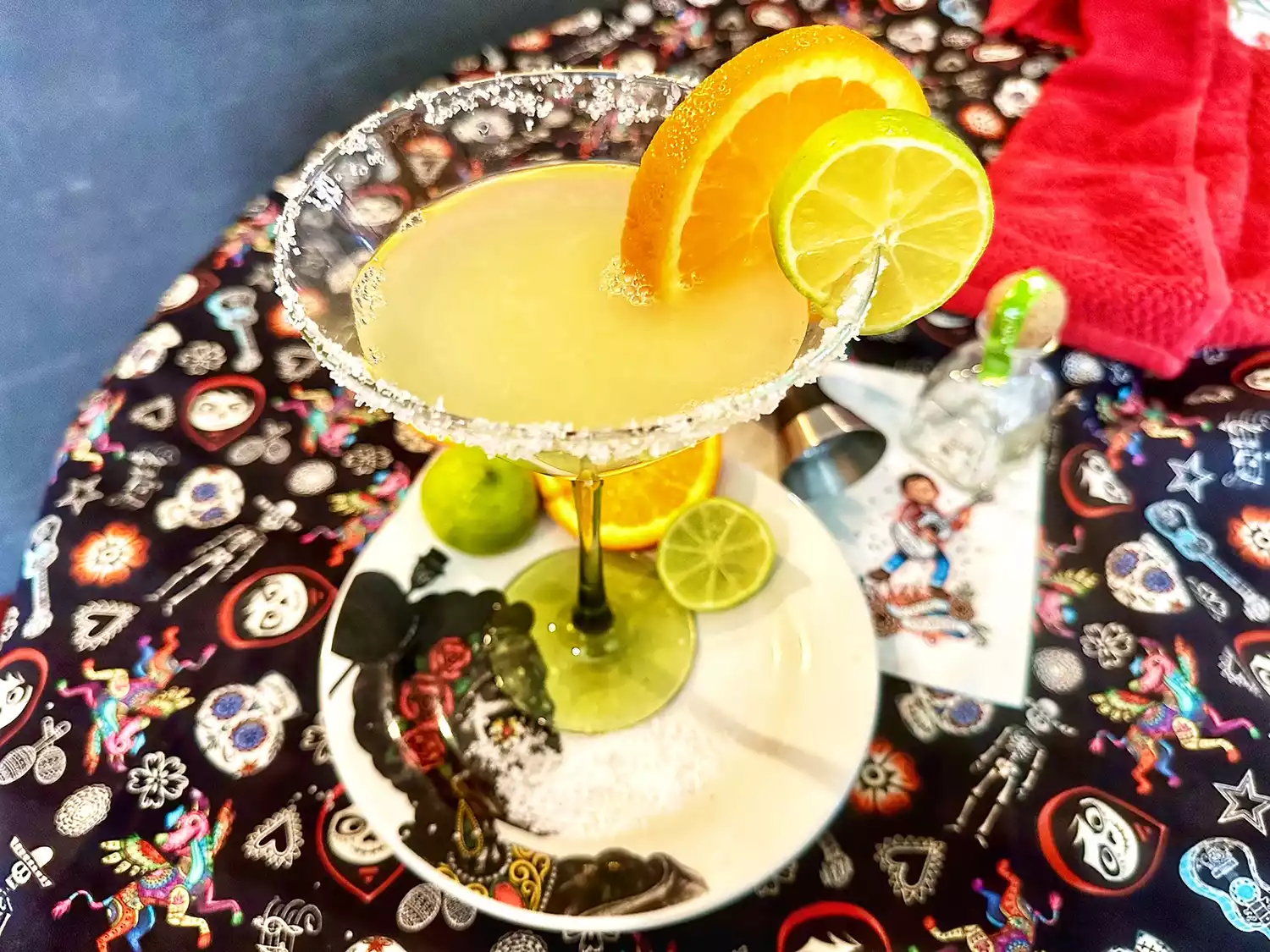 Margarita with fresh orange and lime on saucer with mexican print tablecloth in background