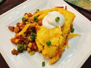 Overhead view of plated cornbread taco casserole with sour cream and green onion