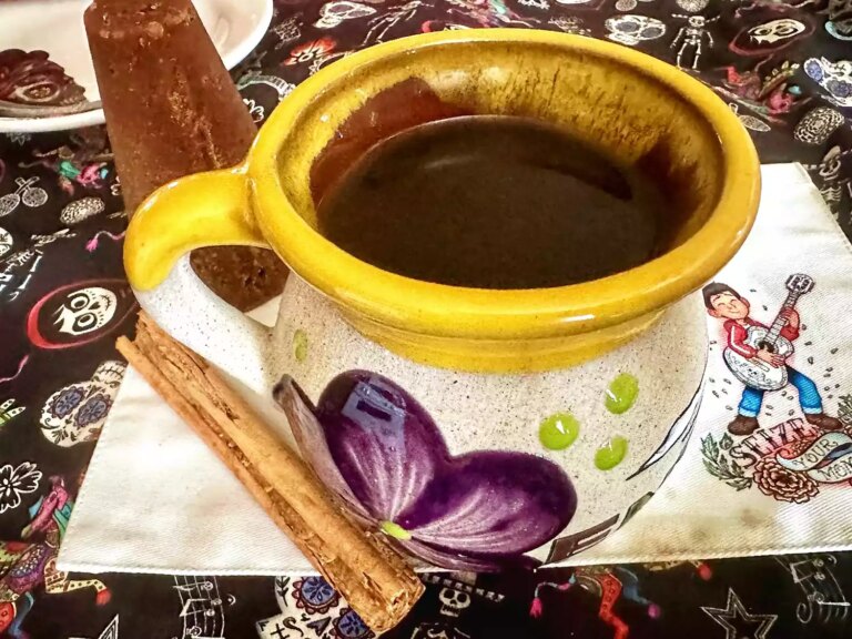 Beautifully painted mexican cup with coffee, cinnamon stick, and piloncillo