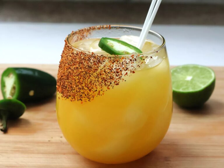 Stemless wine glass with mango margarita, salted with tajin, limes and jalapenos in background