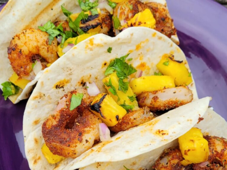 Two grilled pineapple and blackened shrimp tacos on purple plate