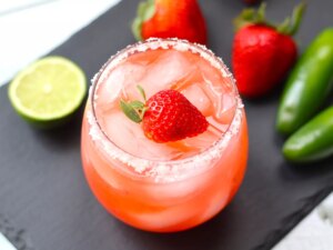 Overhead view of salted rim margarita with jalapenos and strawberries in background