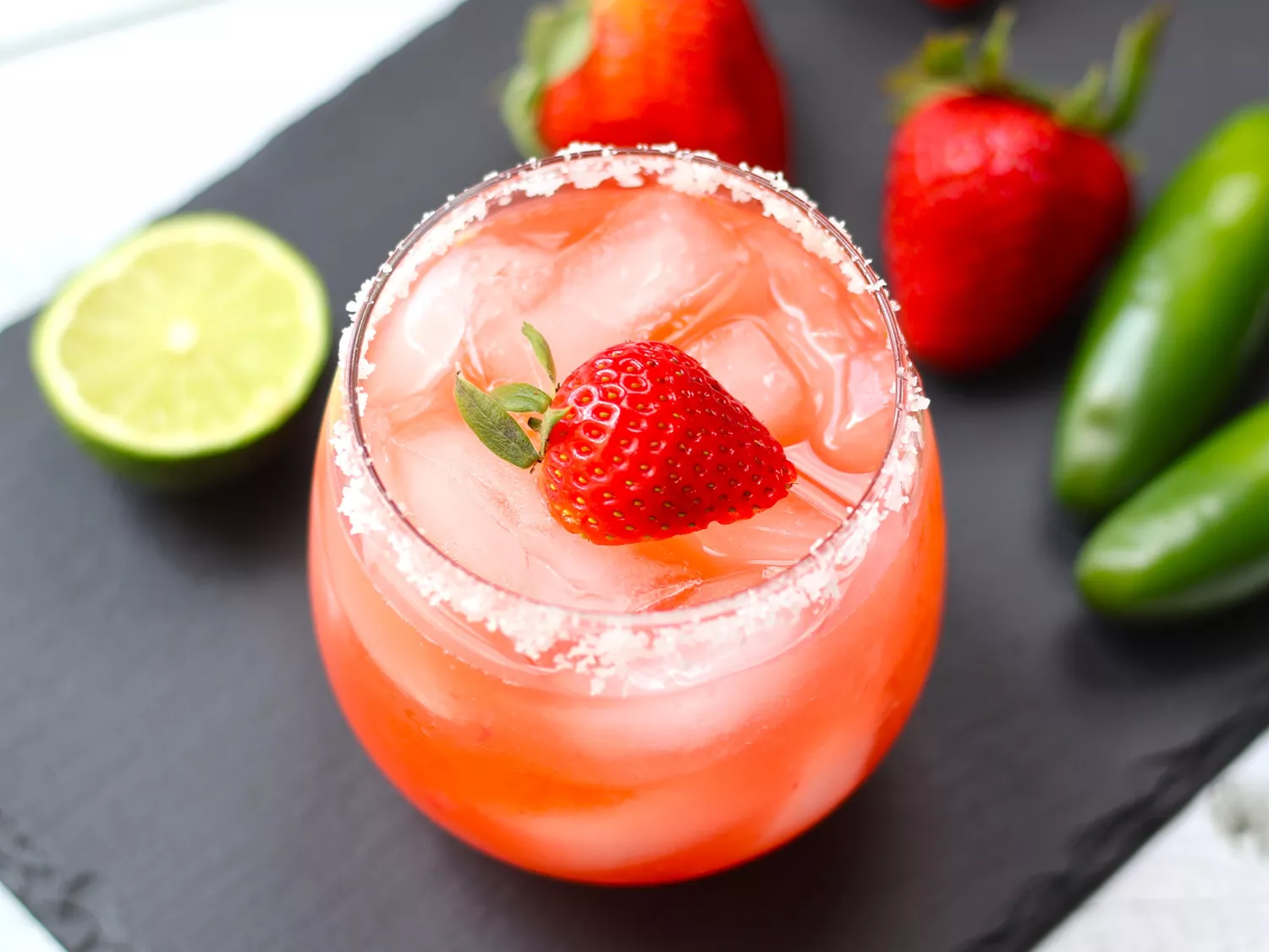 Overhead view of salted rim margarita with jalapenos and strawberries in background