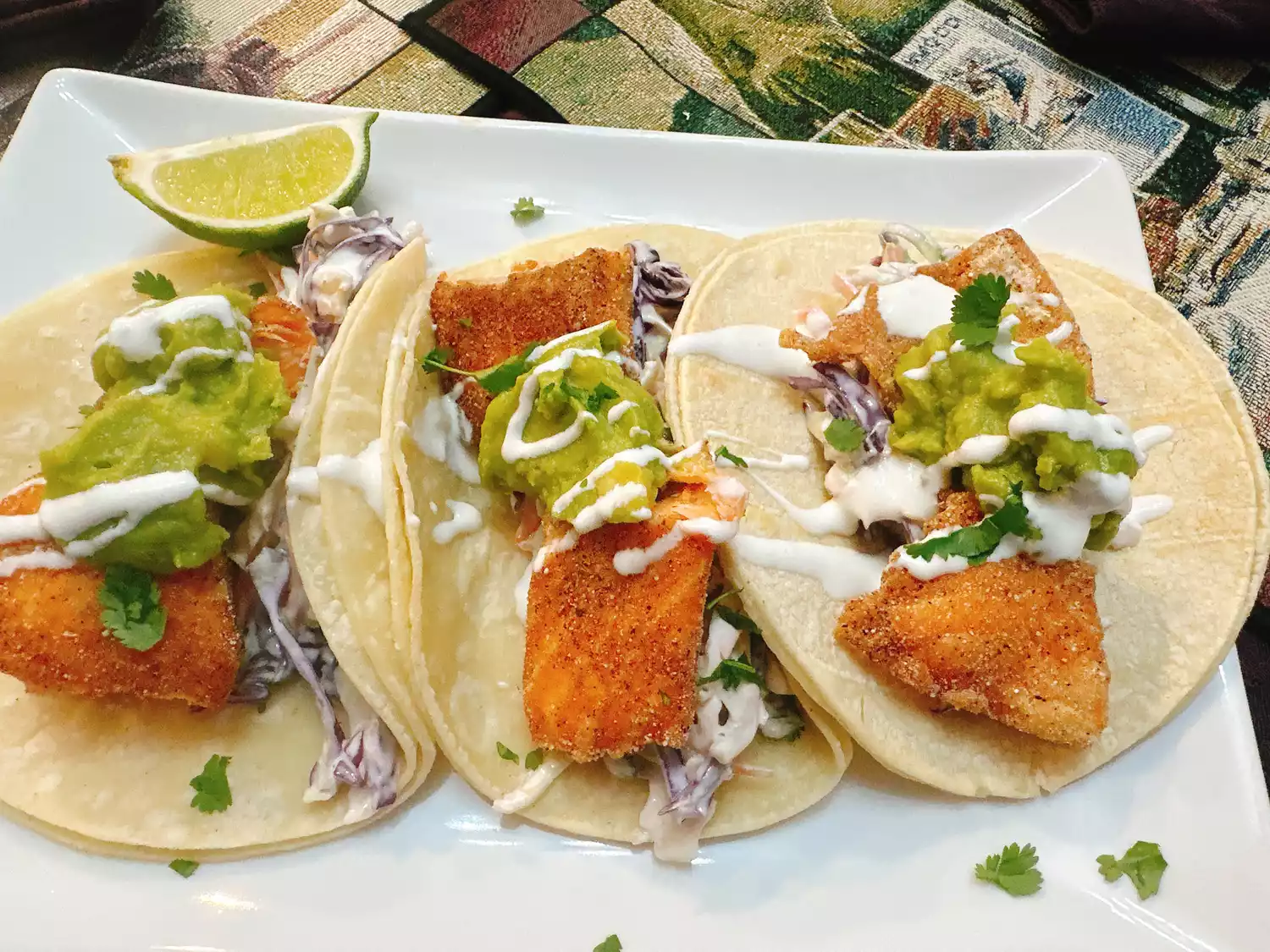 3 fried trout tacos with guacamole and slaw on white square plate